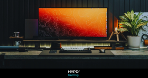 A minimalist desk setup featuring an ultrawide monitor displaying an orange and red contour map design. The desk includes a mechanical keyboard, a mouse, and neatly organised accessories. Decor elements include a potted plant, a vintage-style lamp, and subtle lighting that enhances the warm and modern aesthetic of the space.