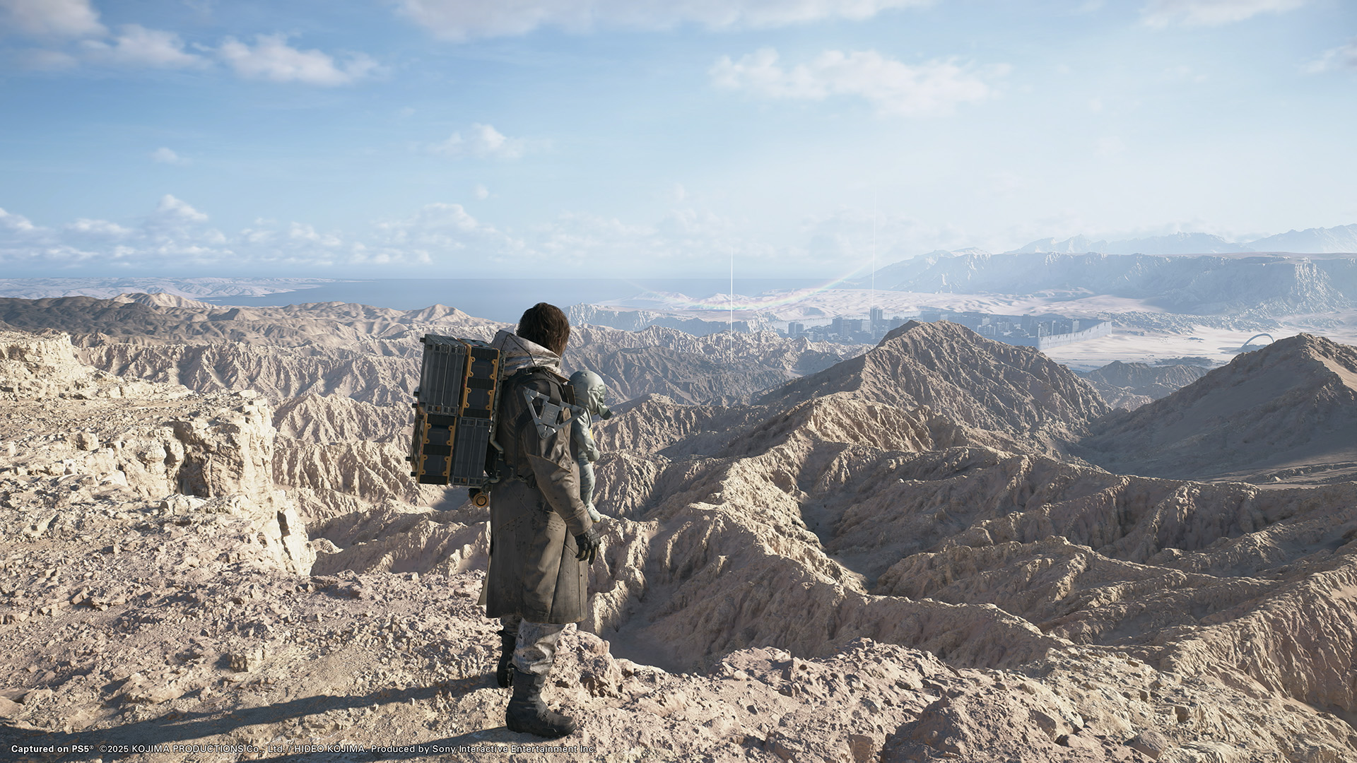 Sam Porter Bridges overlooking a vast rocky desert with his cargo and BB companion in Death Stranding 2: On the Beach.
