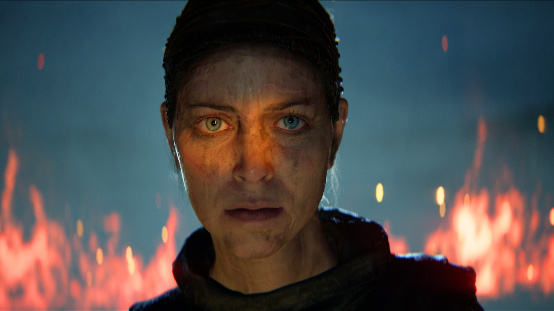 Close-up of Senua’s determined face in Hellblade II with fire glowing in the background
