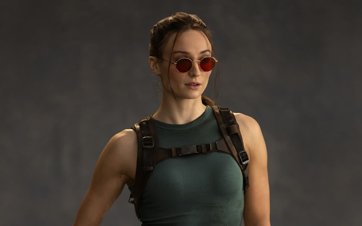 Live-action portrayal of Lara Croft wearing her classic Tomb Raider outfit with tactical harness and sunglasses