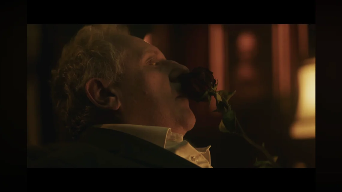 Cinematic scene from Layers of Fear 3 showing a man in a dimly lit room holding a red rose, highlighting the game’s psychological horror atmosphere.