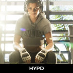 Lucia from GTA 6 sitting in a gym wearing boxing gloves and workout clothing, featured in the latest Grand Theft Auto 6 leaks coverage.