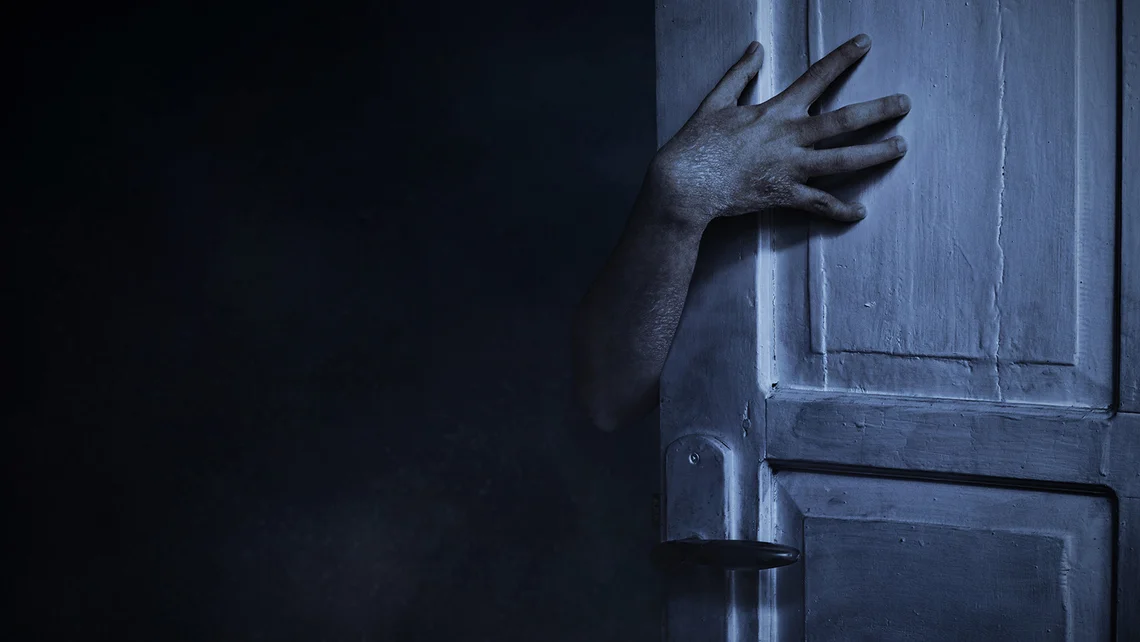 Ghostly hand reaching around a dark doorway, illustrating Phasmophobia's horror gameplay and returning Crimson Eye Halloween event.